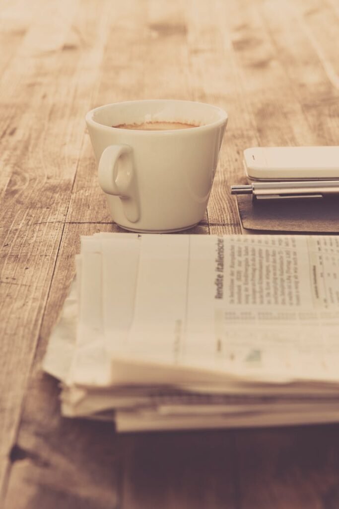 A warm vintage morning setup with coffee, newspaper, and smartphone on wooden table.