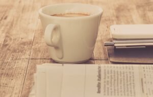 A warm vintage morning setup with coffee, newspaper, and smartphone on wooden table.